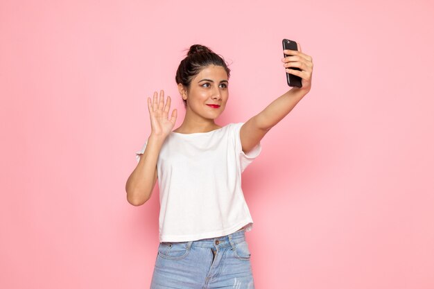 Eine junge Frau der Vorderansicht im weißen T-Shirt und in den blauen Jeans, die ein Selfie nehmen