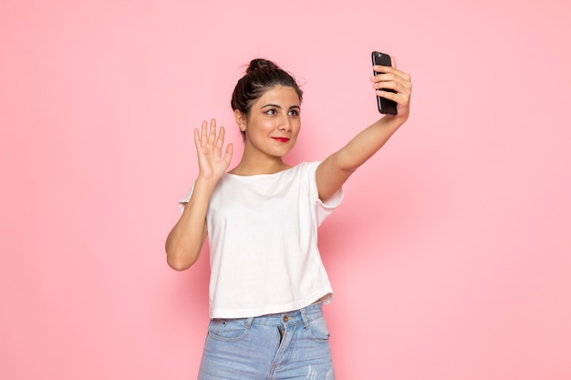 Eine junge Frau der Vorderansicht im weißen T-Shirt und in den blauen Jeans, die ein Selfie nehmen