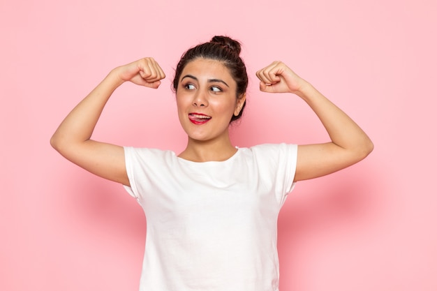 Eine junge Frau der Vorderansicht im weißen T-Shirt und in den blauen Jeans, die sich mit Lächeln beugen