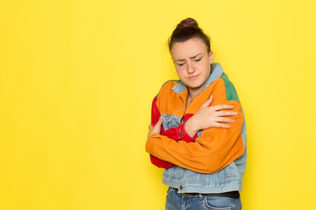 Kostenloses Foto eine junge frau der vorderansicht in der bunten jacke des gelben hemdes und in den blauen jeans, die aufwerfen