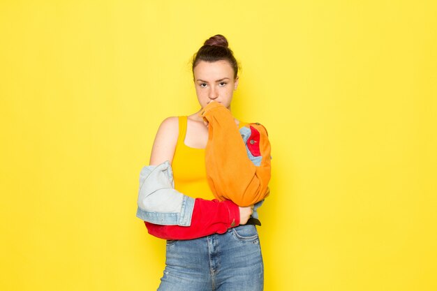 Eine junge Frau der Vorderansicht in der bunten Jacke des gelben Hemdes und in den blauen Jeans, die gerade aufwerfen