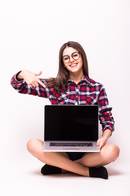 Eine junge Frau, die auf dem Boden saß, zeigte auf Bildschirm mit einem Laptop auf Weiß