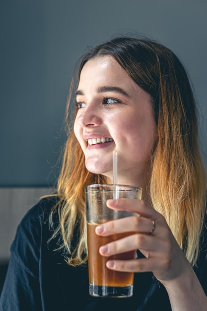 Eine junge Frau, die kaltes Sommerkaffeegetränk mit Eis und Orangensaft trinkt