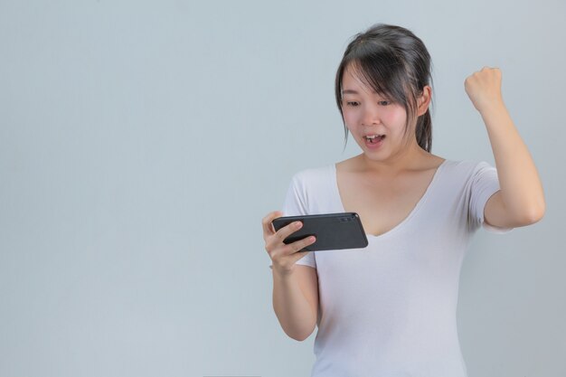 Eine junge Frau, die mit einem Telefon spielt, das Freude an einer grauen Wand zeigt
