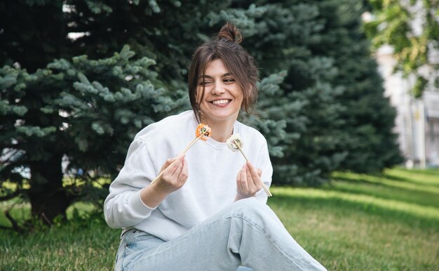 Eine junge Frau, die Sushi im Parkpicknick in der Natur isst