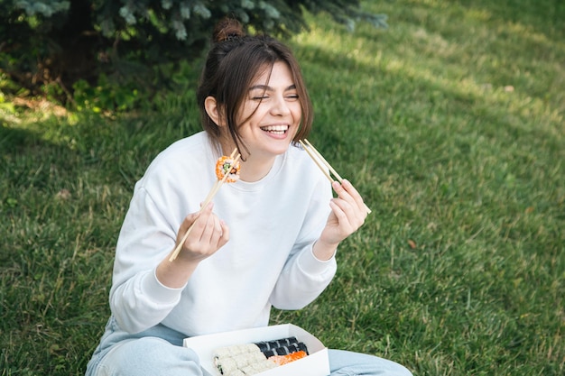 Eine junge Frau, die Sushi im Parkpicknick in der Natur isst