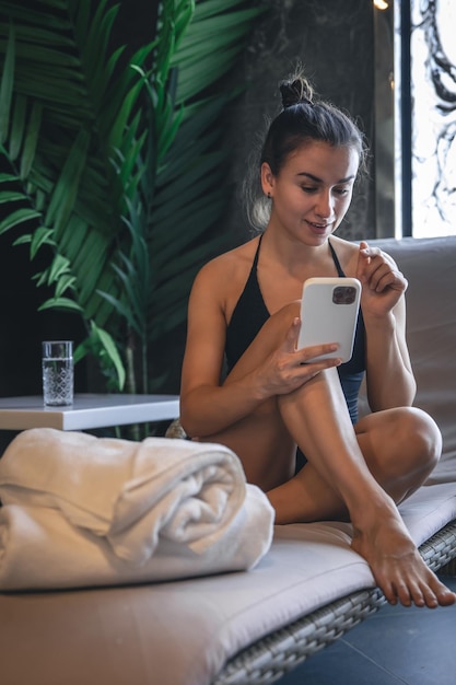 Eine junge frau entspannt sich in einem spa-komplex und benutzt ein smartphone