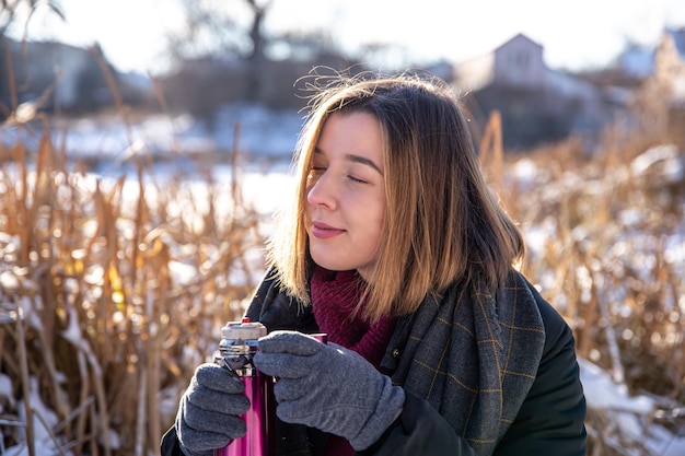 Eine junge Frau genießt bei einem Spaziergang im Winter ein heißes Getränk aus einer Thermoskanne