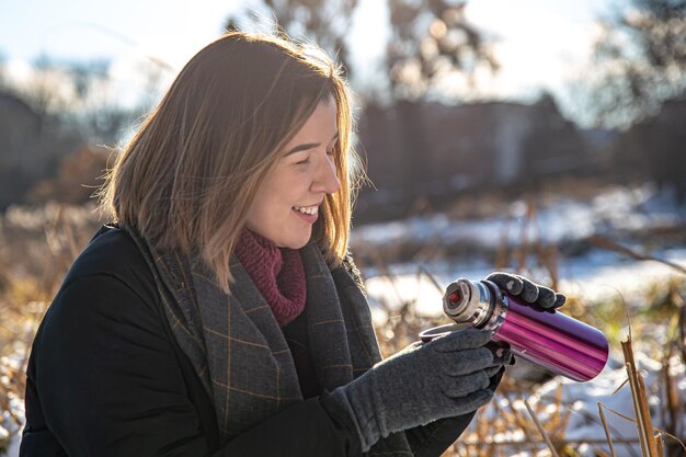 Eine junge Frau genießt bei einem Spaziergang im Winter ein heißes Getränk aus einer Thermoskanne