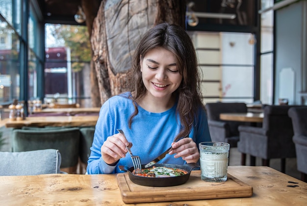 Eine junge Frau in einem Café isst traditionelle Shakshuka und Ayran