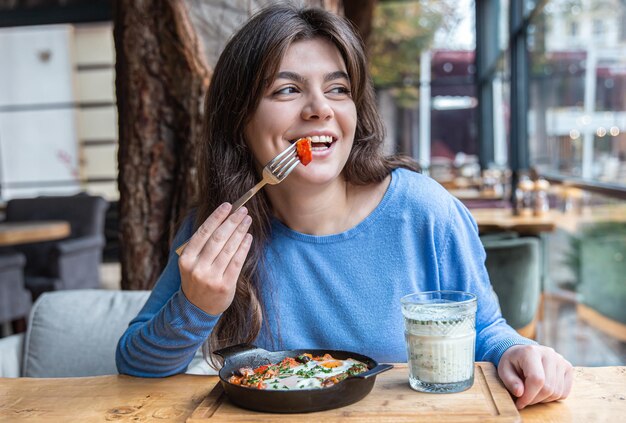 Eine junge Frau in einem Café isst traditionelle Shakshuka und Ayran