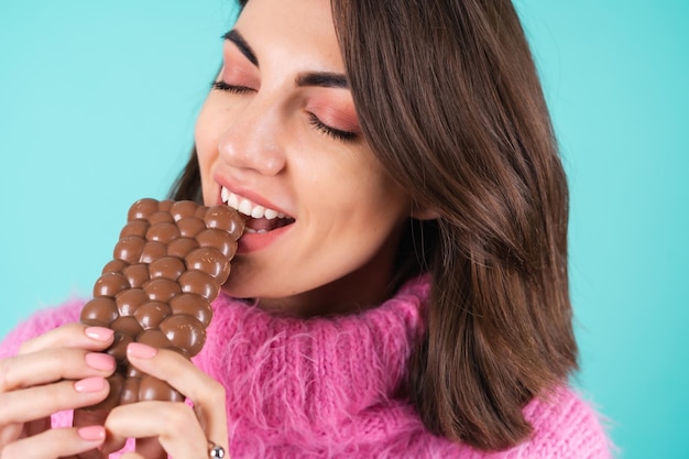 Kostenloses Foto eine junge frau in einem knallbunten pullover auf blau genießt jedes stück einer köstlichen tafel luftiger milchschokolade