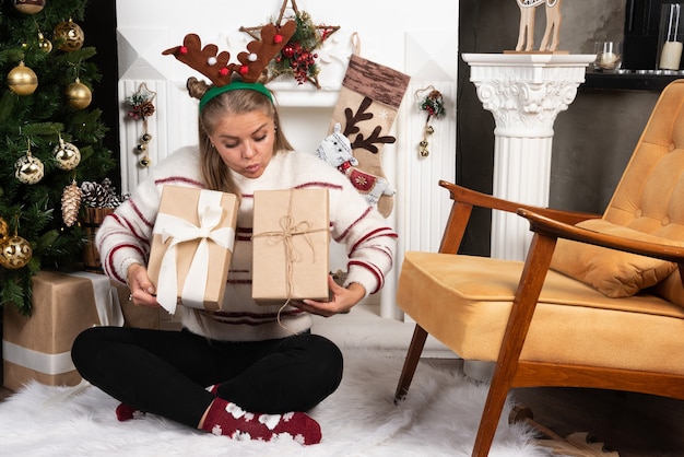 Eine junge Frau in Rotwildohren, die zwei Weihnachtsgeschenke betrachtet.