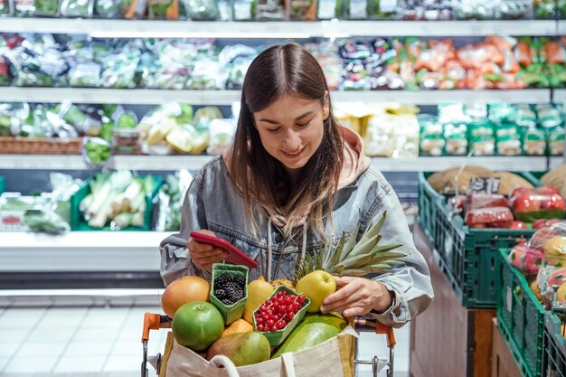 Eine junge Frau kauft Lebensmittel in einem Supermarkt mit einem Telefon in der Hand