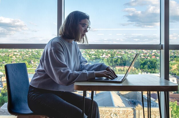 Eine junge Frau mit Brille arbeitet hinter einem Laptop am Arbeitsplatz