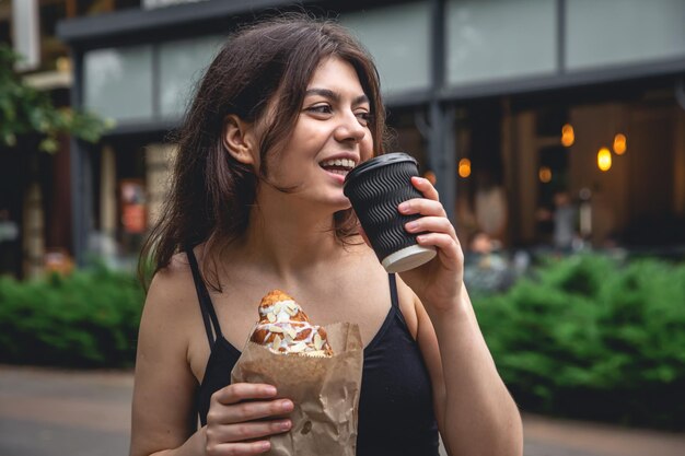 Eine junge Frau mit einem Croissant und einer Tasse Kaffee auf einem Stadtspaziergang