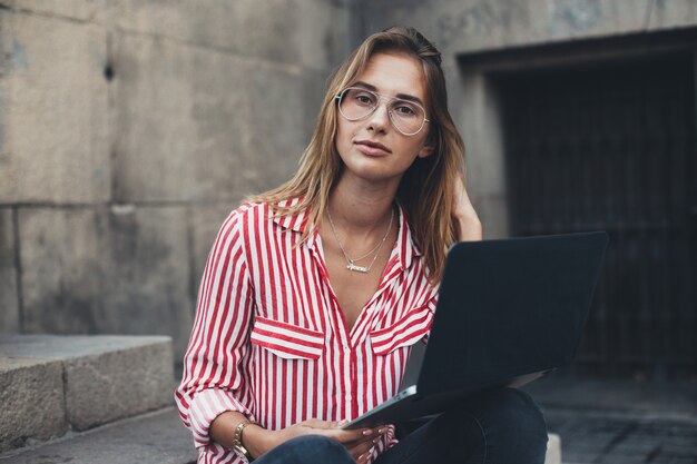 Eine junge frau mit einem laptop sitzt auf der treppe in der nähe der universität