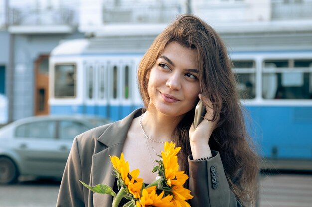 Eine junge Frau mit einem Strauß Sonnenblumen telefoniert bei Sonnenuntergang