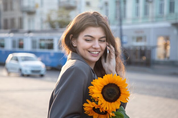 Eine junge Frau mit einem Strauß Sonnenblumen telefoniert bei Sonnenuntergang