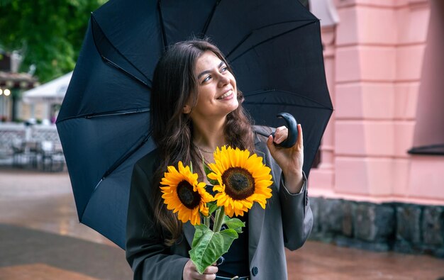 Eine junge Frau mit einem Strauß Sonnenblumen unter einem Regenschirm bei Regenwetter