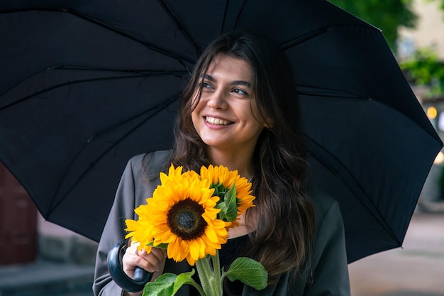 Eine junge Frau mit einem Strauß Sonnenblumen unter einem Regenschirm bei Regenwetter