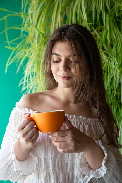 Eine junge frau mit einer tasse kaffee im hintergrund mit grünen pflanzen