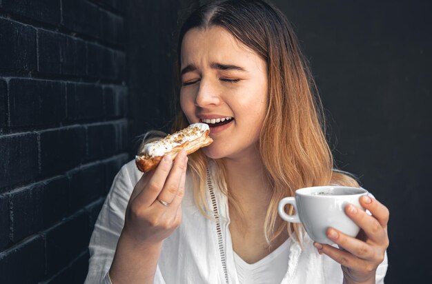 Eine junge Frau mit einer Tasse Kaffee und einem Eclair in der Hand