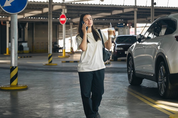 Eine junge Frau mit Kaffee telefoniert auf dem Parkplatz