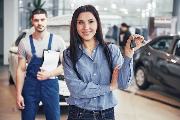 Eine junge Frau nimmt ein Auto vom Autowerkstatt. Sie ist glücklich, weil die Arbeit perfekt gemacht ist