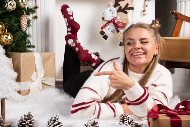 Eine junge Frau posiert auf Teppich im Weihnachtsinnenraum liegend.