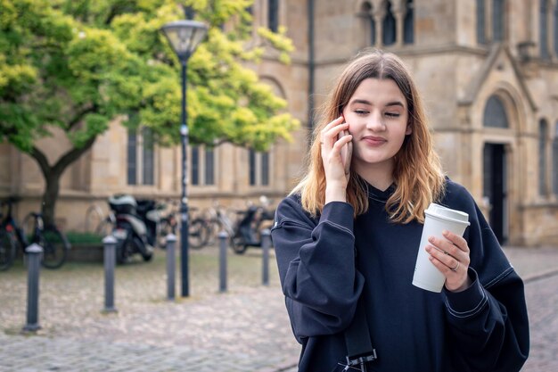 Eine junge Frau trinkt Kaffee und telefoniert bei einem Spaziergang in der Stadt