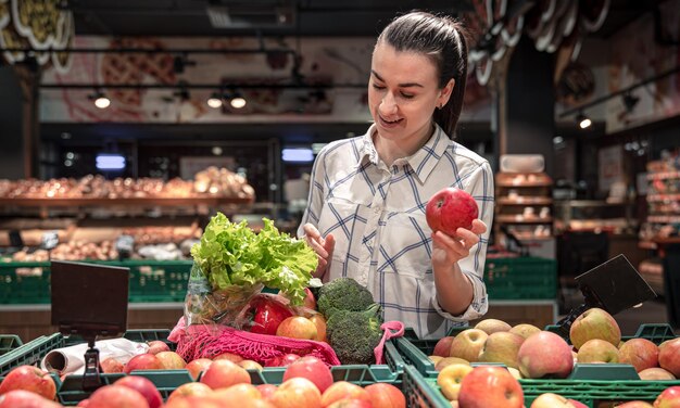 Eine junge Frau wählt in einem Supermarkt Obst und Gemüse aus