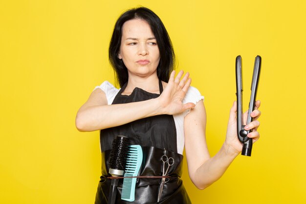 Eine junge Friseurin der Vorderansicht im weißen Umhang des weißen Umhangs des weißen T-Shirts, der Haar besorgt Werkzeugausdruck hält