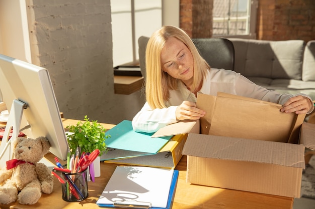 Eine junge Geschäftsfrau zieht ins Büro und bekommt einen neuen Arbeitsplatz. Junge kaukasische Büroangestellte rüstet neues Kabinett nach Beförderung aus. Kisten auspacken. Geschäft, Lebensstil, neues Lebenskonzept.