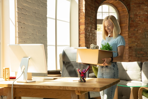 Kostenloses Foto eine junge geschäftsfrau zieht ins büro und bekommt einen neuen arbeitsplatz. junge kaukasische büroangestellte rüstet neues kabinett nach beförderung aus. sieht glücklich aus. geschäft, lebensstil, neues lebenskonzept.