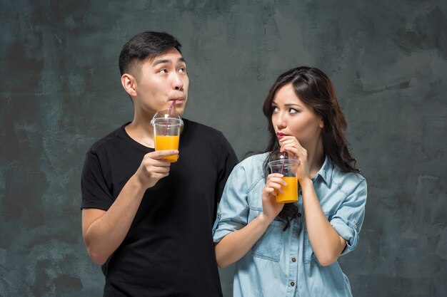 Eine junge hübsche asiatische Frau mit einem Glas Orangensaft in den Händen am grauen Studiohintergrund.