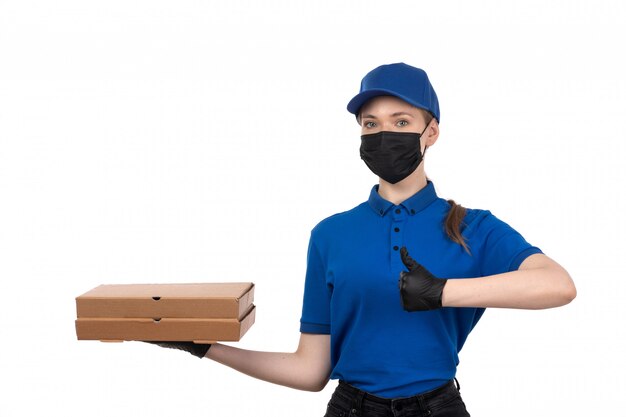 Eine junge Kurierin der Vorderansicht in der blauen Maske der blauen Uniform und in den Handschuhen, die Lebensmittel-Lieferpakete halten