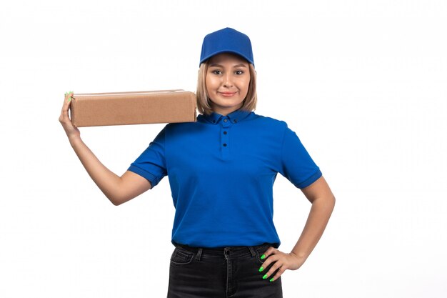 Eine junge Kurierin der Vorderansicht in der blauen Uniform, die Lebensmittel-Lieferpaket mit Lächeln auf ihrem Gesicht hält