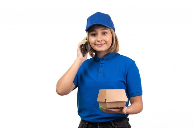 Eine junge Kurierin der Vorderansicht in der blauen Uniform, die Telefon- und Lebensmittellieferpaket hält