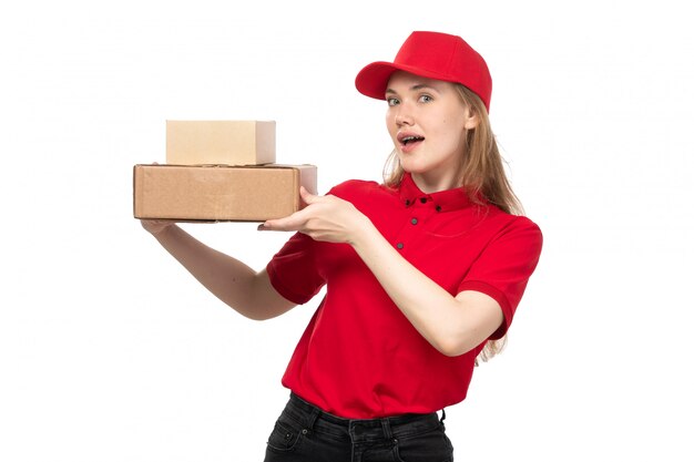 Eine junge Kurierin der Vorderansicht weiblicher Arbeiter des Lebensmittel-Lieferservices lächelnd, das Kisten mit Essen auf Weiß hält