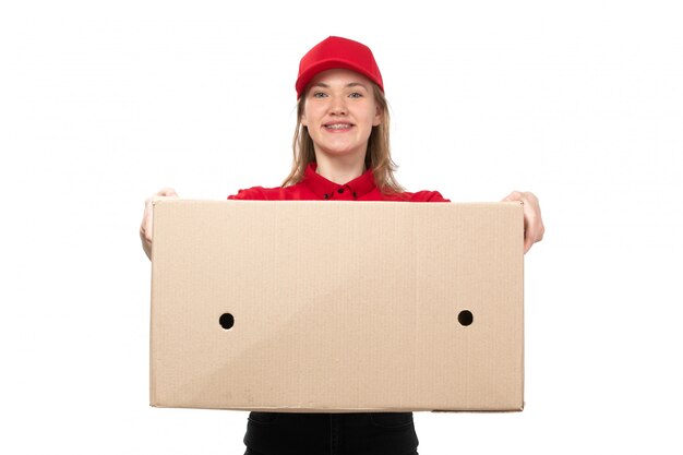 Eine junge Kurierin der Vorderansicht weiblicher Arbeiter des Lebensmittellieferservice lächelnd, der eine riesige Lieferbox auf Weiß hält