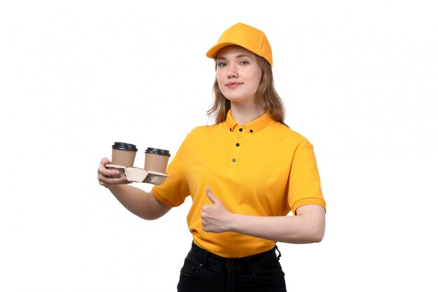 Eine junge Kurierin der Vorderansicht weiblicher Arbeiter des Lebensmittellieferservices, der Kaffeetassen mit Lächeln auf ihrem Gesicht auf Weiß hält