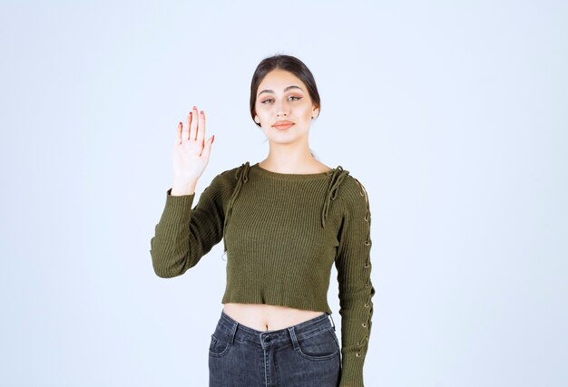 Eine junge lächelnde Frau im grünen Pullover, die eine Hand winkt.