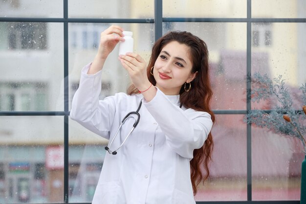 Eine junge Mitarbeiterin des Gesundheitswesens, die eine Medikamentenkapsel hält und sie ansieht Foto in hoher Qualität