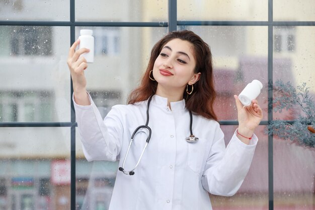 Eine junge Mitarbeiterin des Gesundheitswesens, die eine Medikamentenkapsel hält und sie ansieht Foto in hoher Qualität