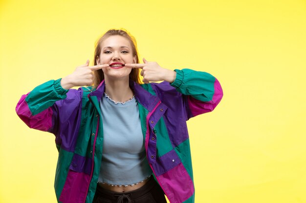 Eine junge moderne Frau der Vorderansicht in der bunten Jacke der blauen Hose des schwarzen Hemdes lächelnd posierend