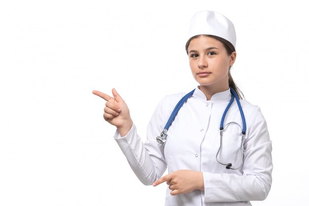 Eine junge Ärztin der Vorderansicht im weißen medizinischen Anzug mit dem blauen Stethoskop, das aufwirft