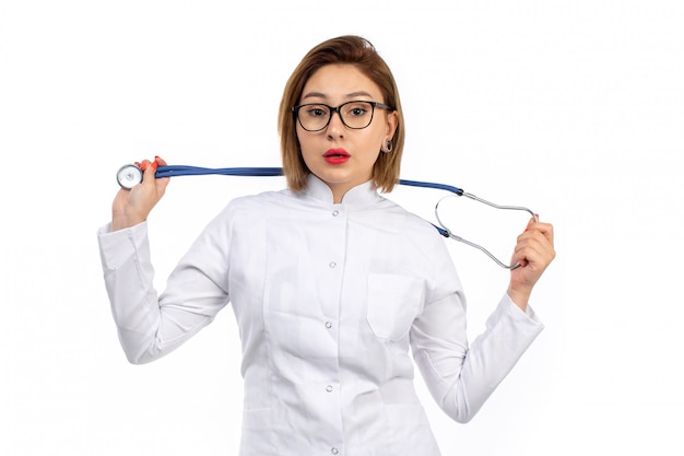 Eine junge Ärztin der Vorderansicht im weißen medizinischen Anzug mit Stethoskop auf dem Weiß