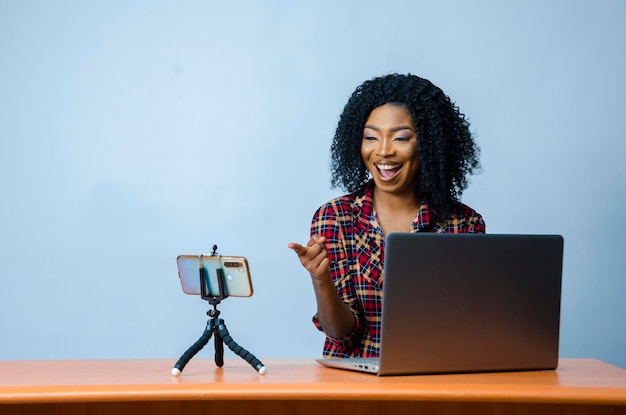 Eine junge schöne afrikanische geschäftsfrau isoliert über weißem hintergrund, die sich aufgeregt fühlt, während sie ihren laptop bedient und mit ihrem handy einen videoanruf tätigt