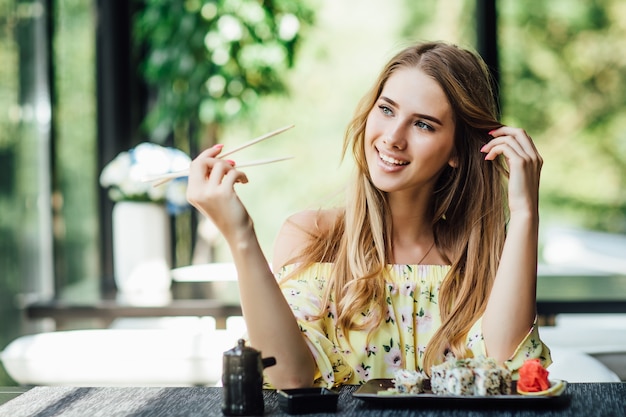 Eine junge schöne blonde, hübsche Frau isst Sushi auf der Sommerterrasse eines japanischen Restaurants